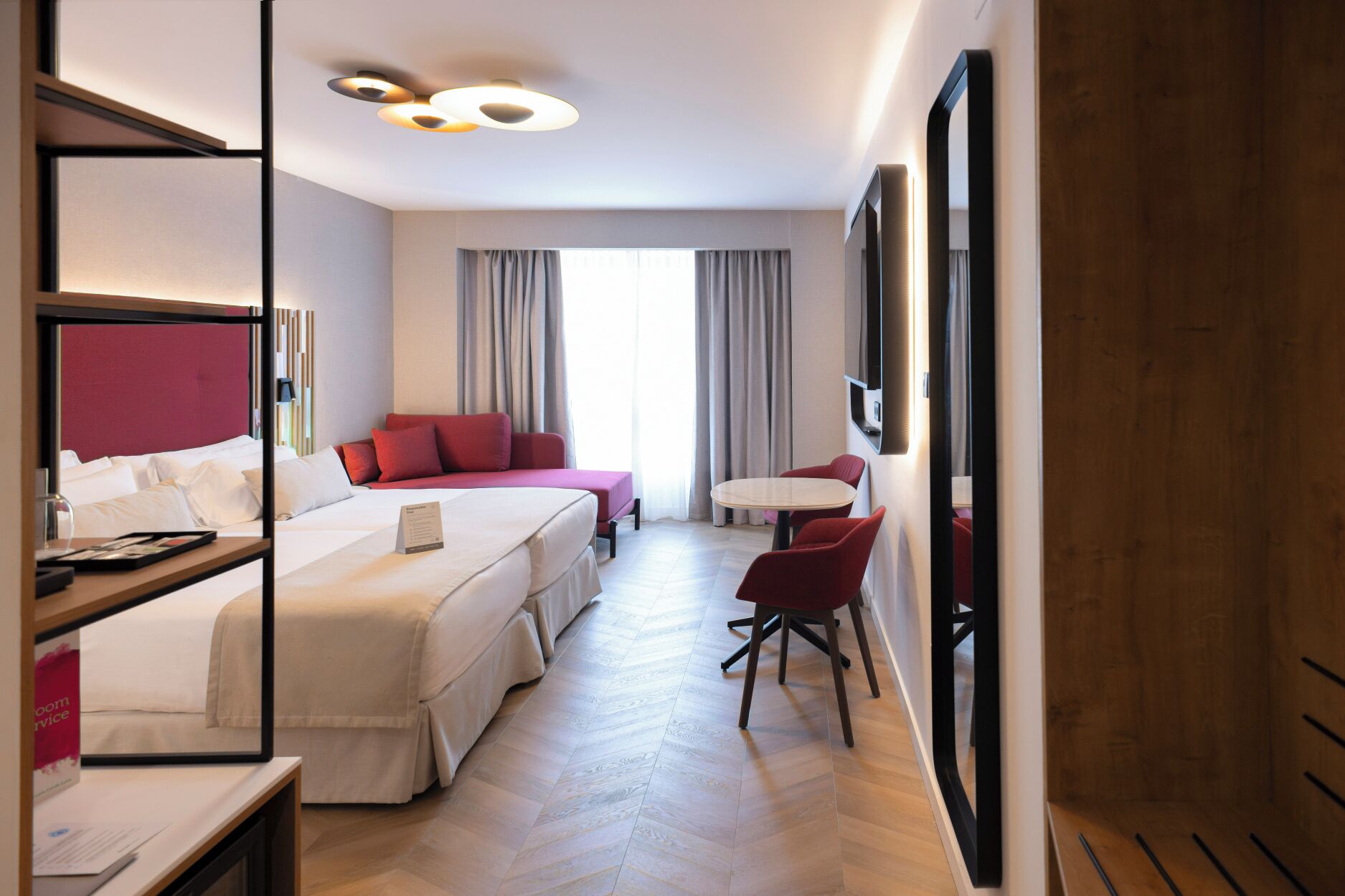 A hotel room with a bed, a desk, a chair, a TV, and a window with curtains.