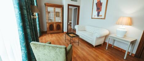 A living room with a wooden floor, a white sofa, a green armchair, a small table, and a lamp.