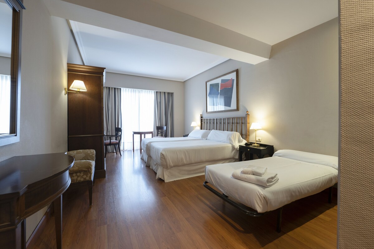Une chambre d’hôtel avec deux lits, un bureau, une chaise et une petite table.