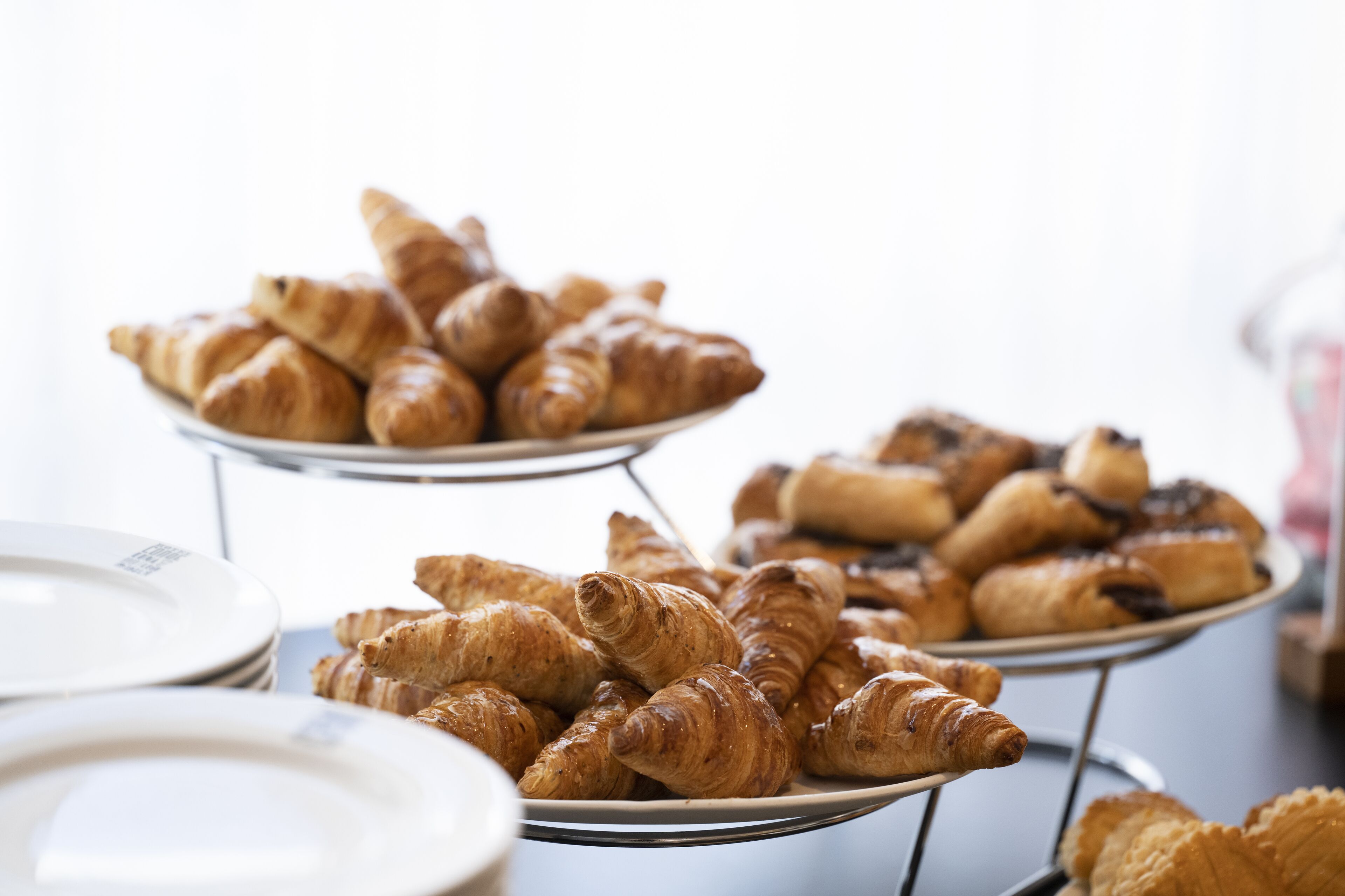A buffet table with various pastries, including croissants and chocolate-covered items, arranged on metal stands.