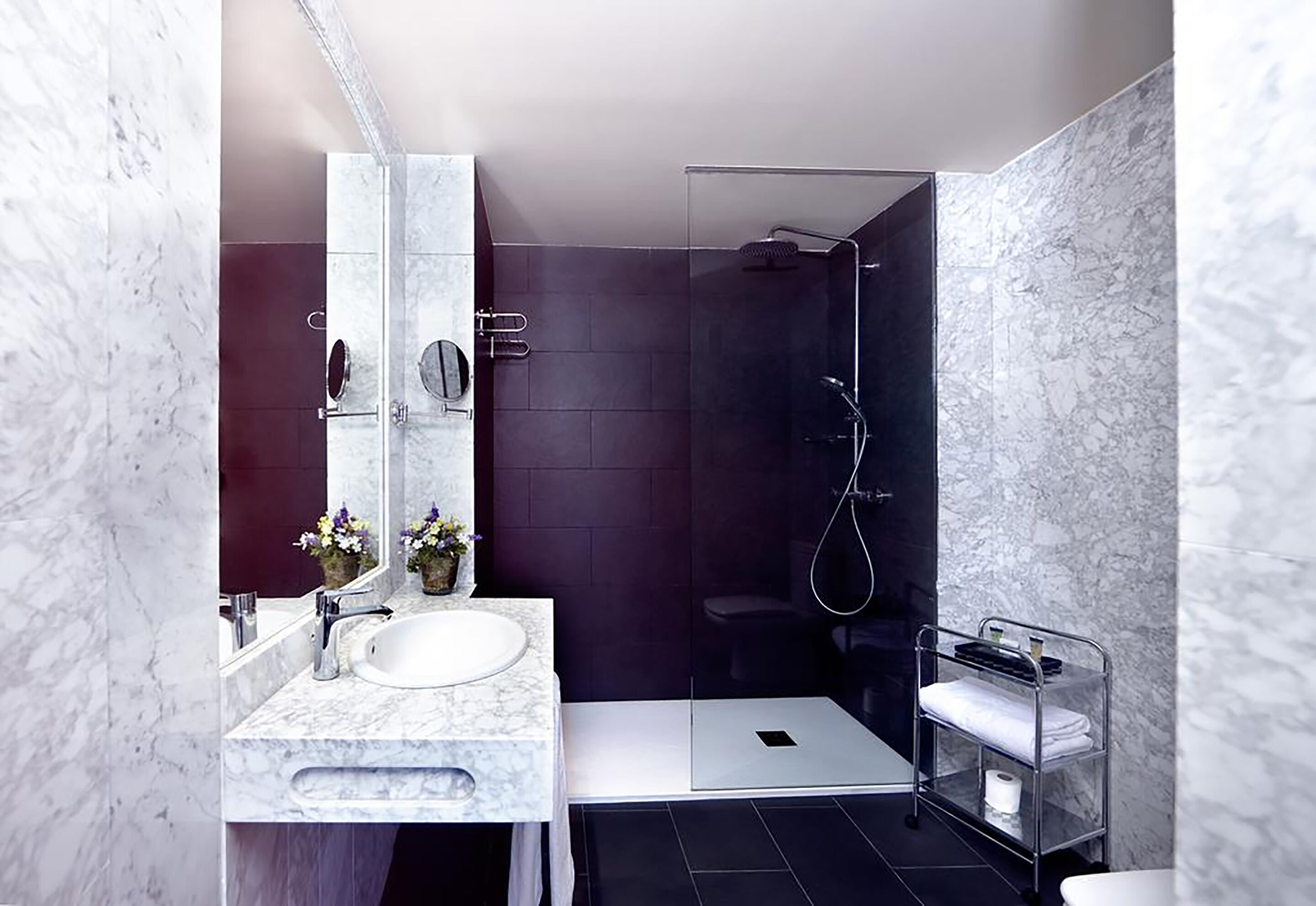 A modern bathroom with a marble sink, a large mirror, a glass shower enclosure, and a metal towel rack.
