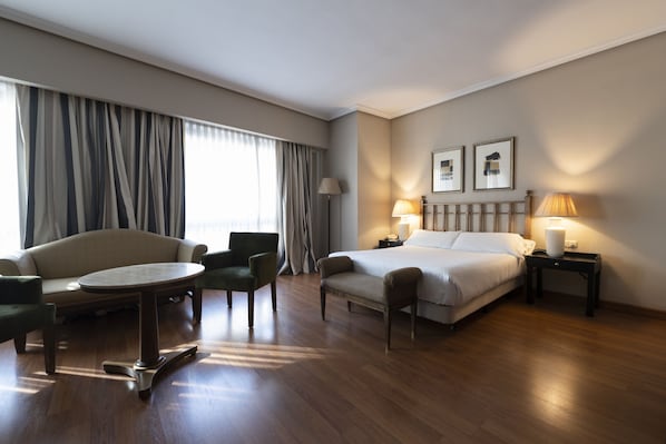 A hotel room with a bed, two chairs, a small table, a lamp, and a picture on the wall.