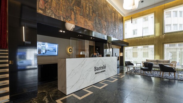 Un área de recepción de hotel moderna con mostrador de mármol, una pantalla digital y un espacio de espera con sofás y sillones.