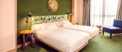 A hotel room with two beds, a green textured wall, a decorative wall piece, a small round table, and a blue chair.