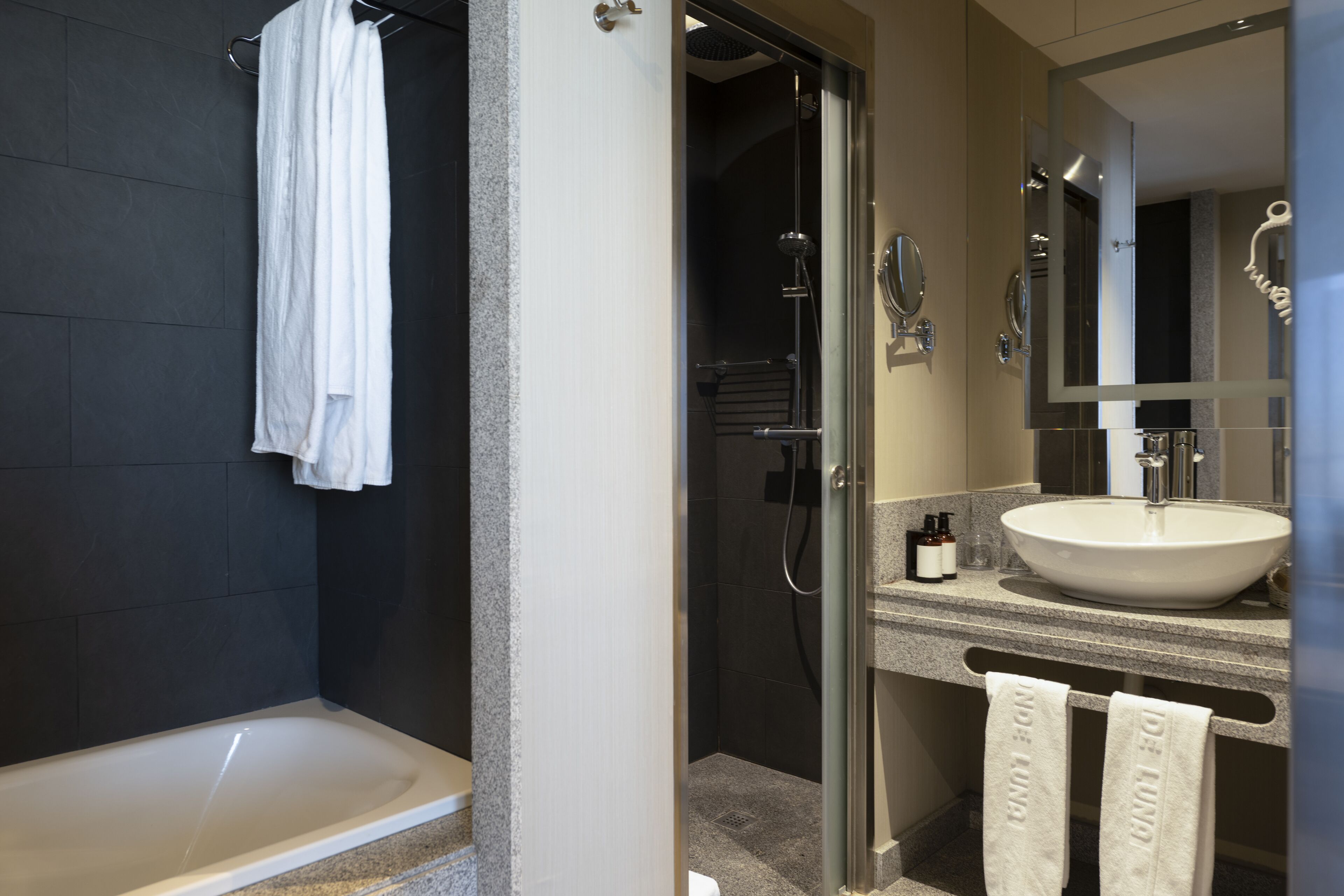 Un baño moderno con bañera, ducha con cerramiento de vidrio y tocador con lavabo y espejo.