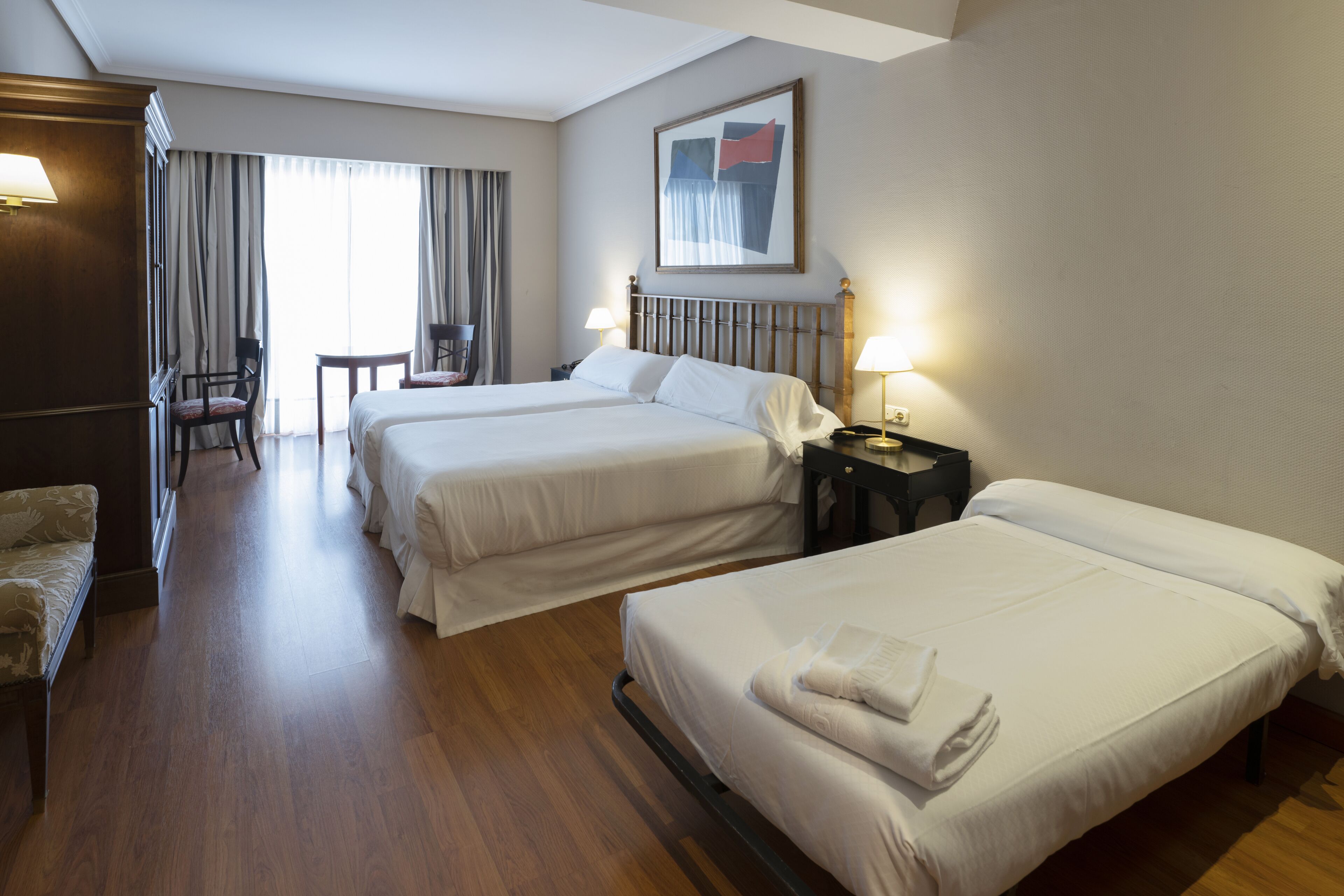 A hotel room with two beds, a desk, a chair, and a window with curtains.