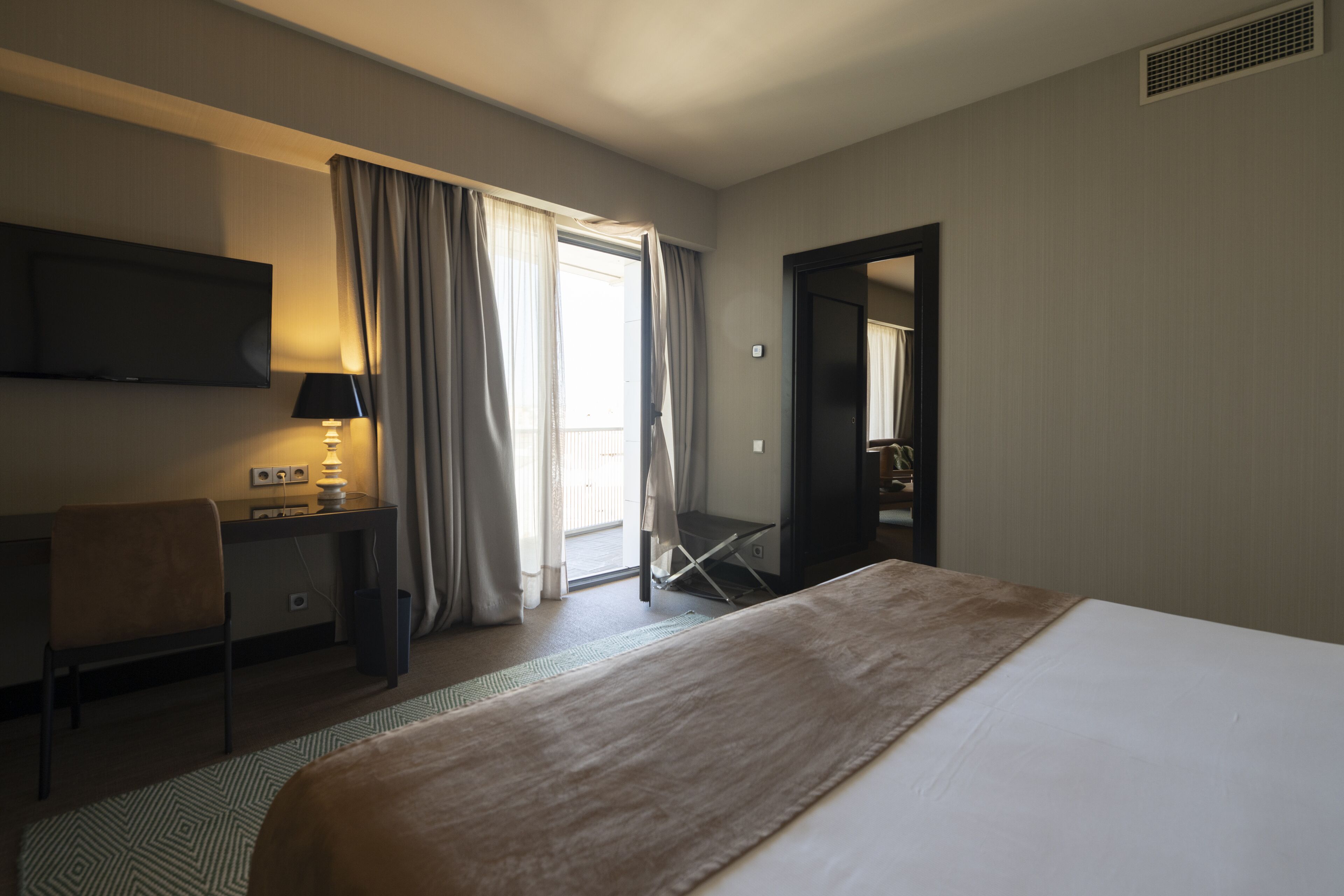 Une chambre d’hôtel équipée d’un lit, d’un bureau, d’une chaise, d’une télévision et d’une porte donnant sur un balcon.