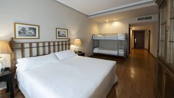 Una habitación de hotel con una cama grande, un cabecero de madera, dos lámparas de noche, una cama individual y cuadros en la pared.