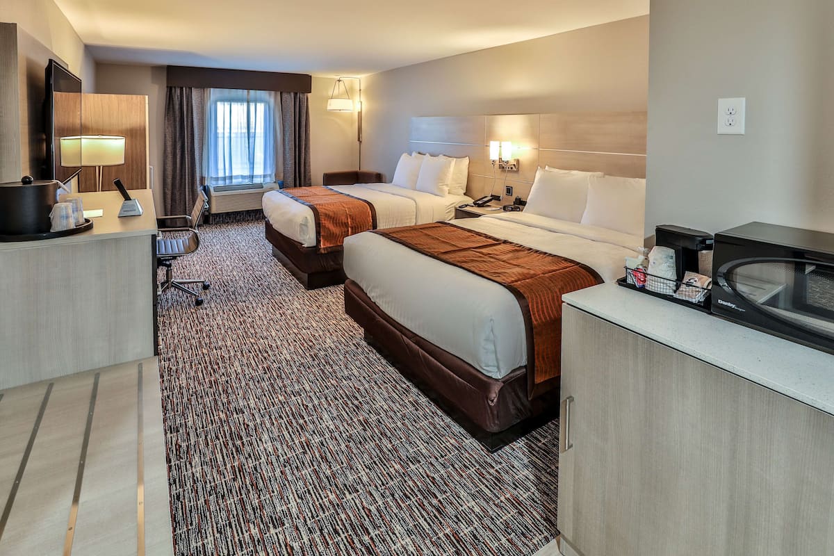 A hotel room with two beds, a desk, a chair, a microwave, and a large window with curtains.