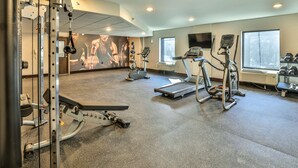 Un gimnasio con máquinas de cardio, equipo de levantamiento de pesas y un espejo grande.