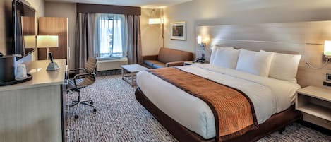 A hotel room with a large bed, a desk with a chair, a sofa, a TV, and a window with curtains.