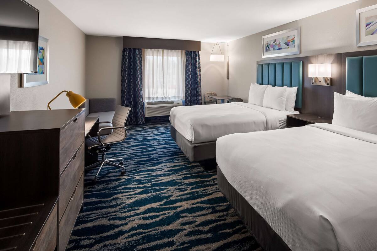 A hotel room with two beds, a desk, a chair, a dresser, and a window with curtains.
