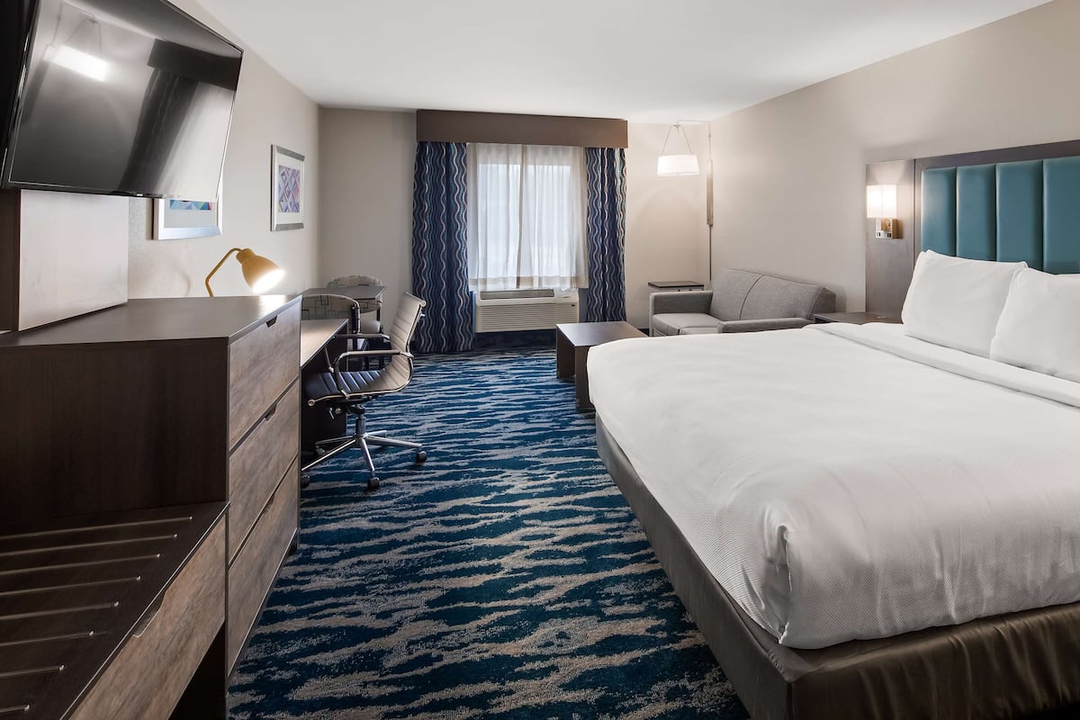 A hotel room with a large bed, a desk with a chair, a TV, and a window with curtains.