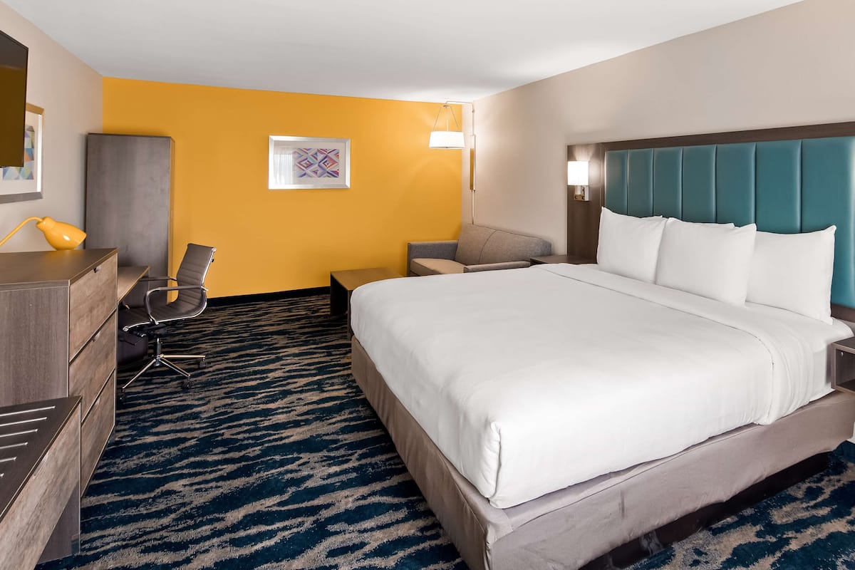 A hotel room with a bed, a desk, a chair, a lamp, and a wall-mounted TV.