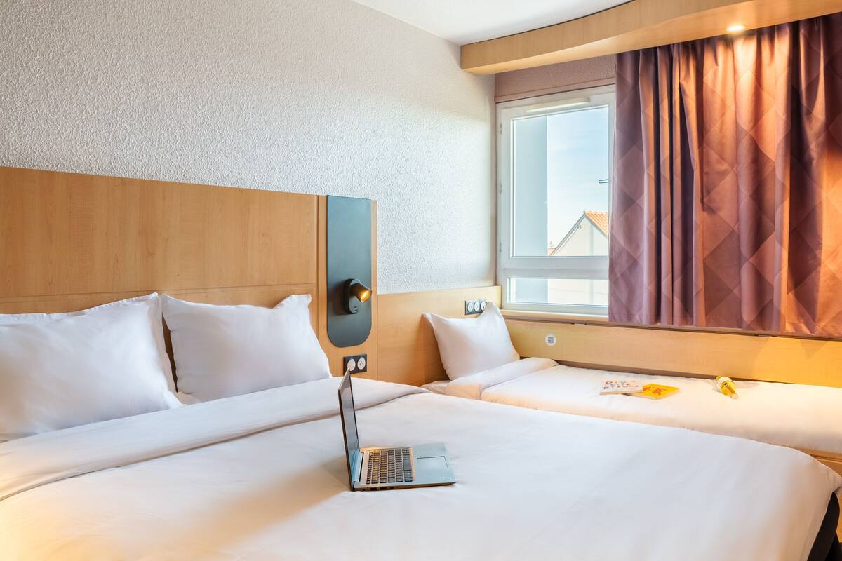 Habitació d'hotel amb dos llits, un portàtil sobre el llit esquerre i una finestra amb cortines.