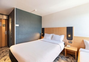 A hotel room with a large bed, a wooden headboard, a nightstand, and a wall-mounted light fixture. - B&B HOTEL Lyon Eurexpo Bron (Bron)