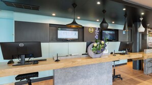 Een receptiebalie met twee monitoren, een bloevas en een bord met 'B&B CLUB'.
