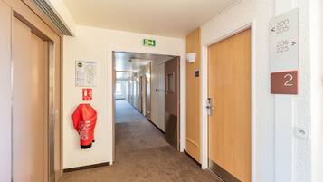 A hotel hallway with numbered doors, an emergency exit sign, and a fire extinguisher.