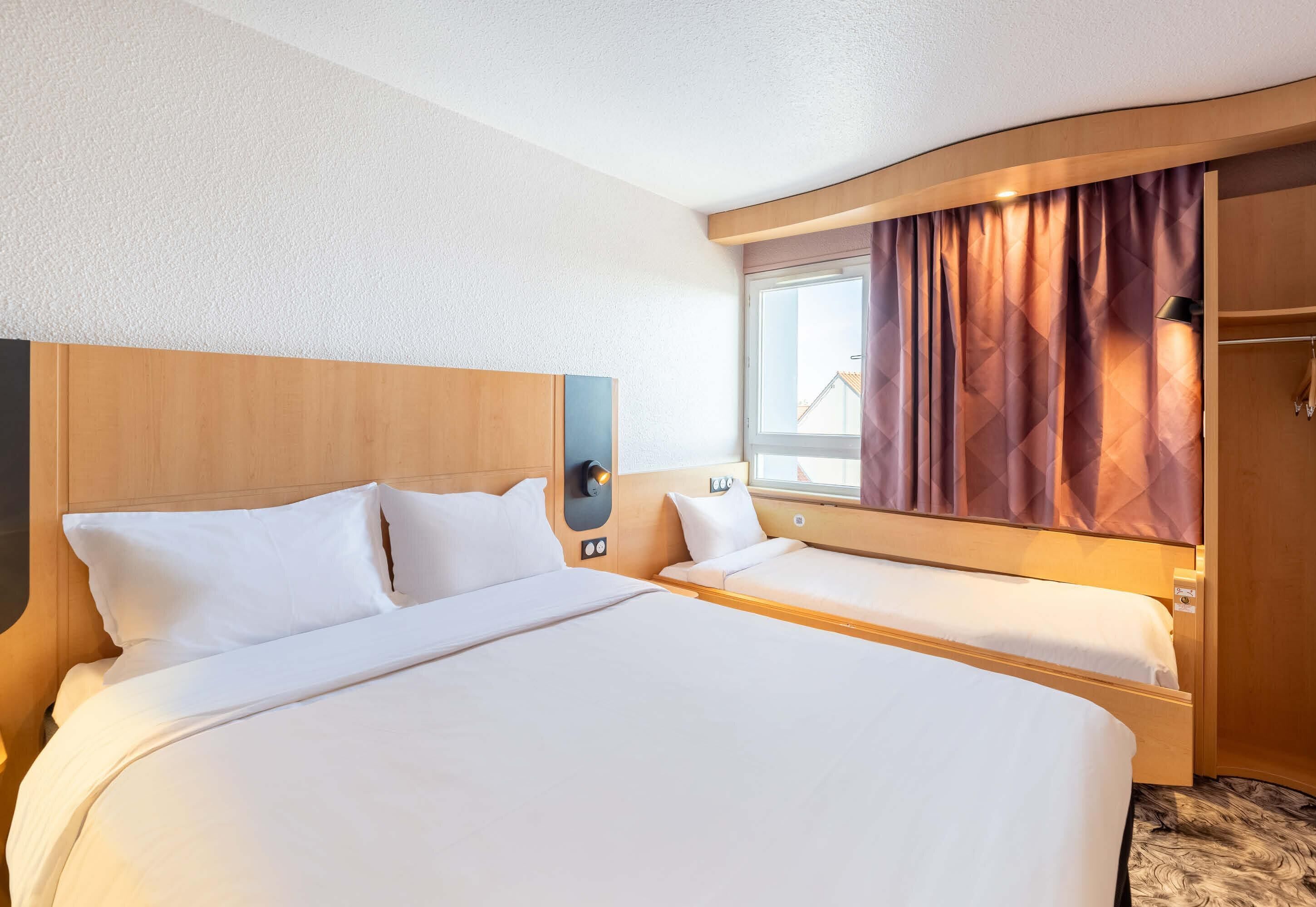 Une chambre d’hôtel avec deux lits, une fenêtre avec des rideaux, une armoire et une table de chevet.