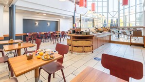 Een ruim café met houten tafels en stoelen, een centrale toonbank met manden, en grote ramen die natuurlijk licht binnenlaten.