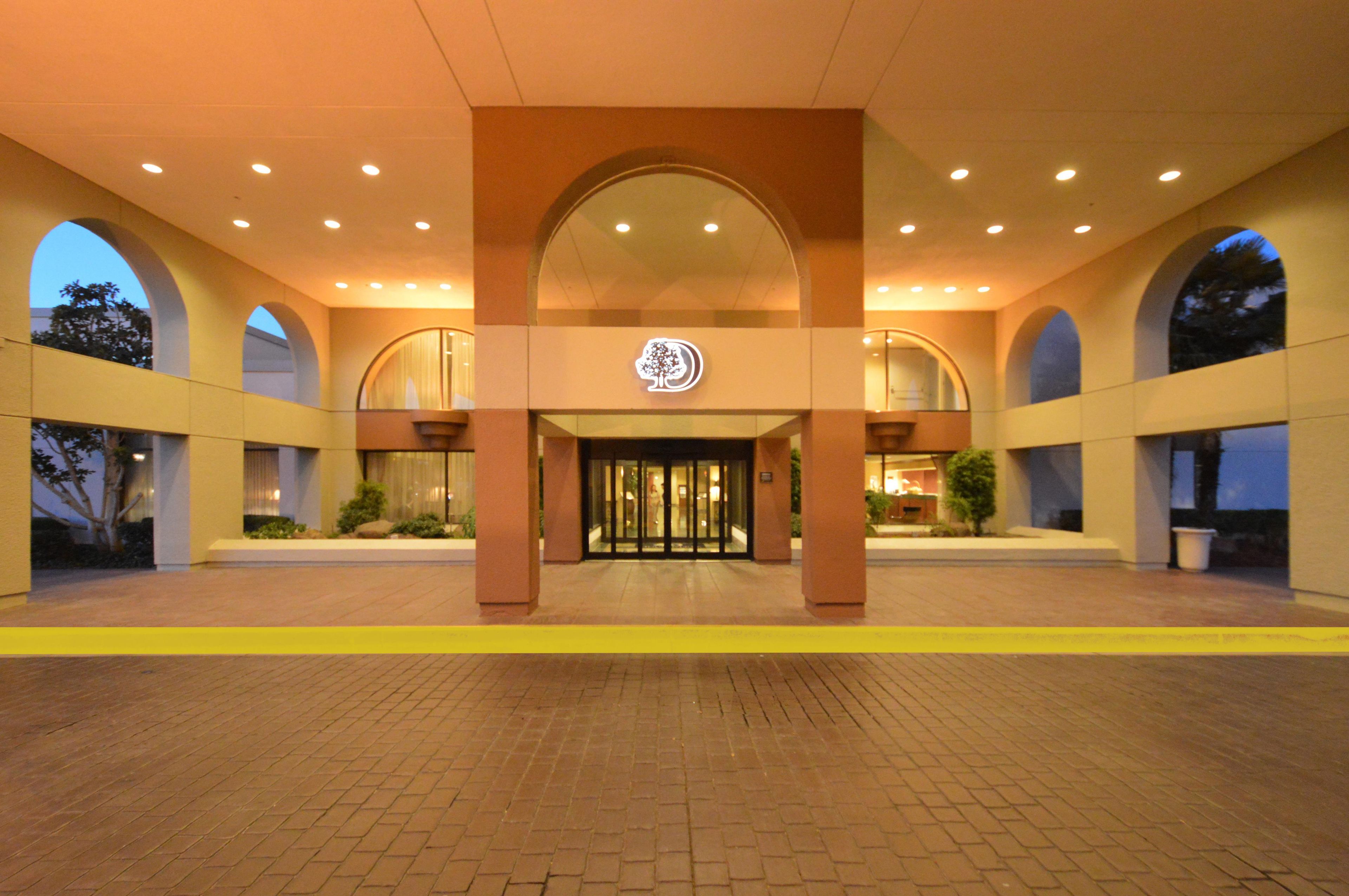 A hotel entrance with a central archway, a logo above the doors, and a brick-paved ground.