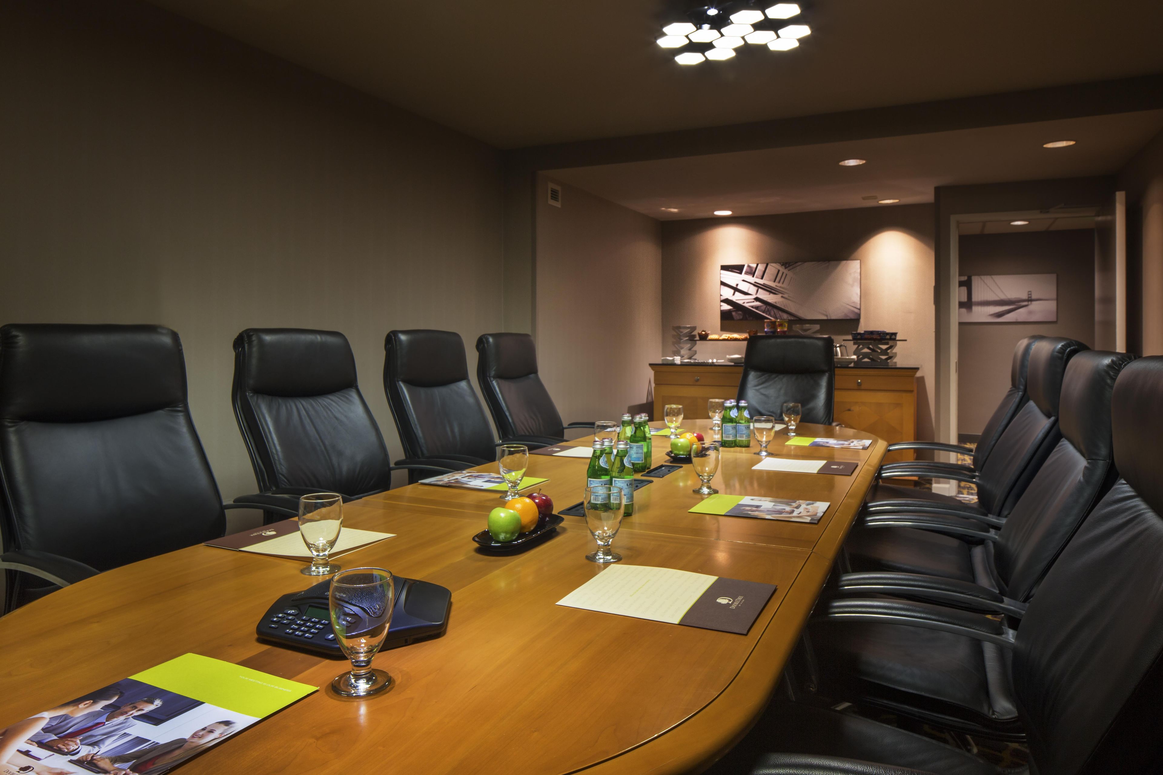 Un salón de conferencias con una mesa larga, varias sillas y una pequeña cocina en el fondo.