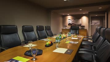 Un salón de conferencias con una mesa larga, varias sillas y una pequeña cocina en el fondo.