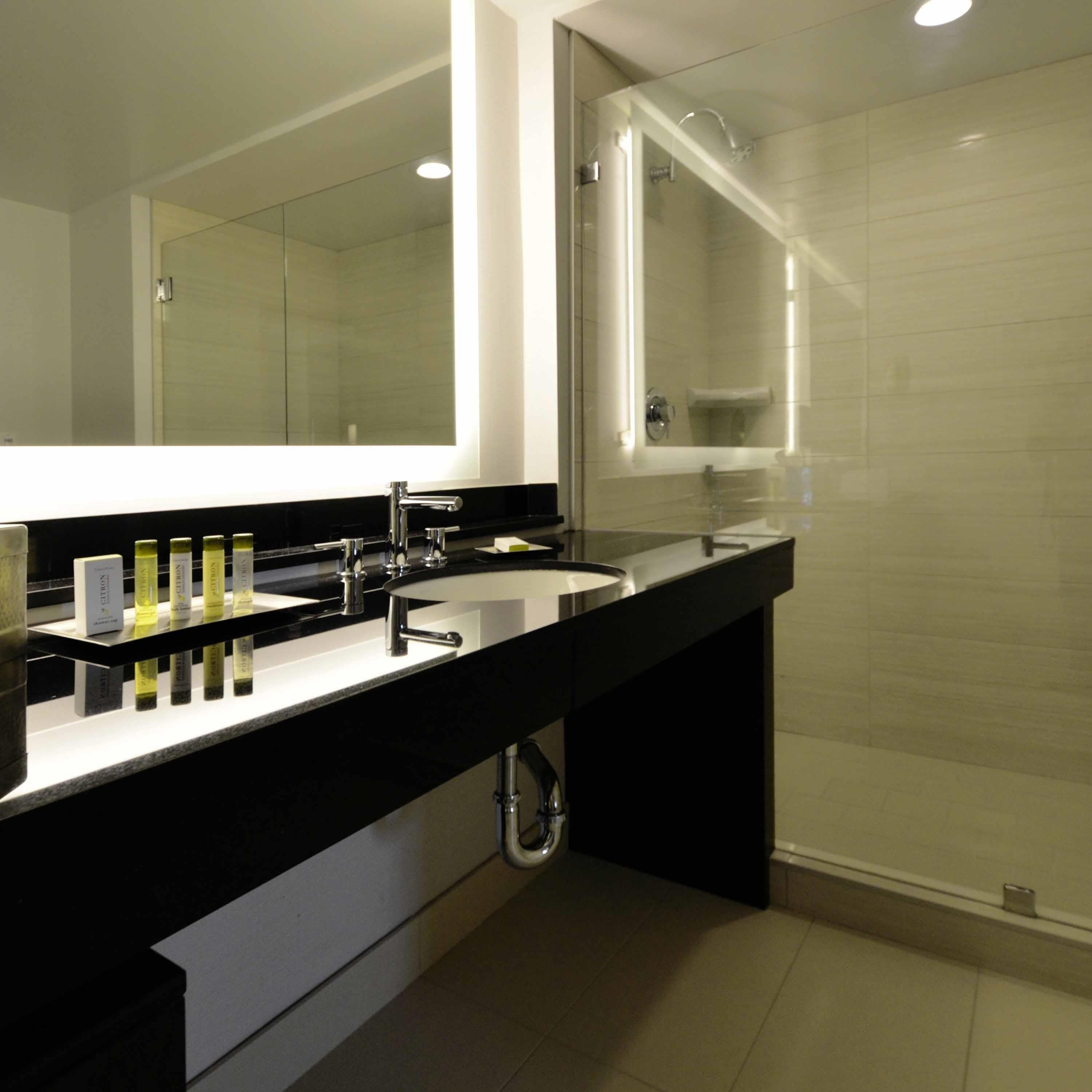 A modern bathroom with a black countertop, a large mirror, and a glass-enclosed shower.