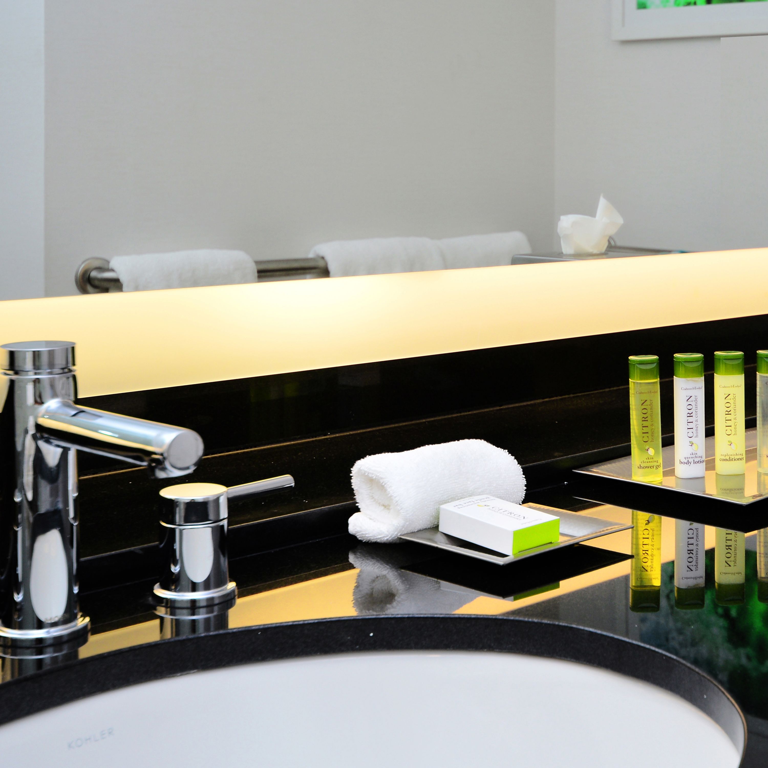 A modern bathroom with a black countertop, a chrome faucet, and a glass shelf holding toiletries.