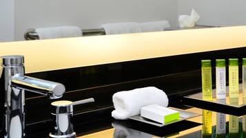 A modern bathroom with a black countertop, a chrome faucet, and a glass shelf holding toiletries.