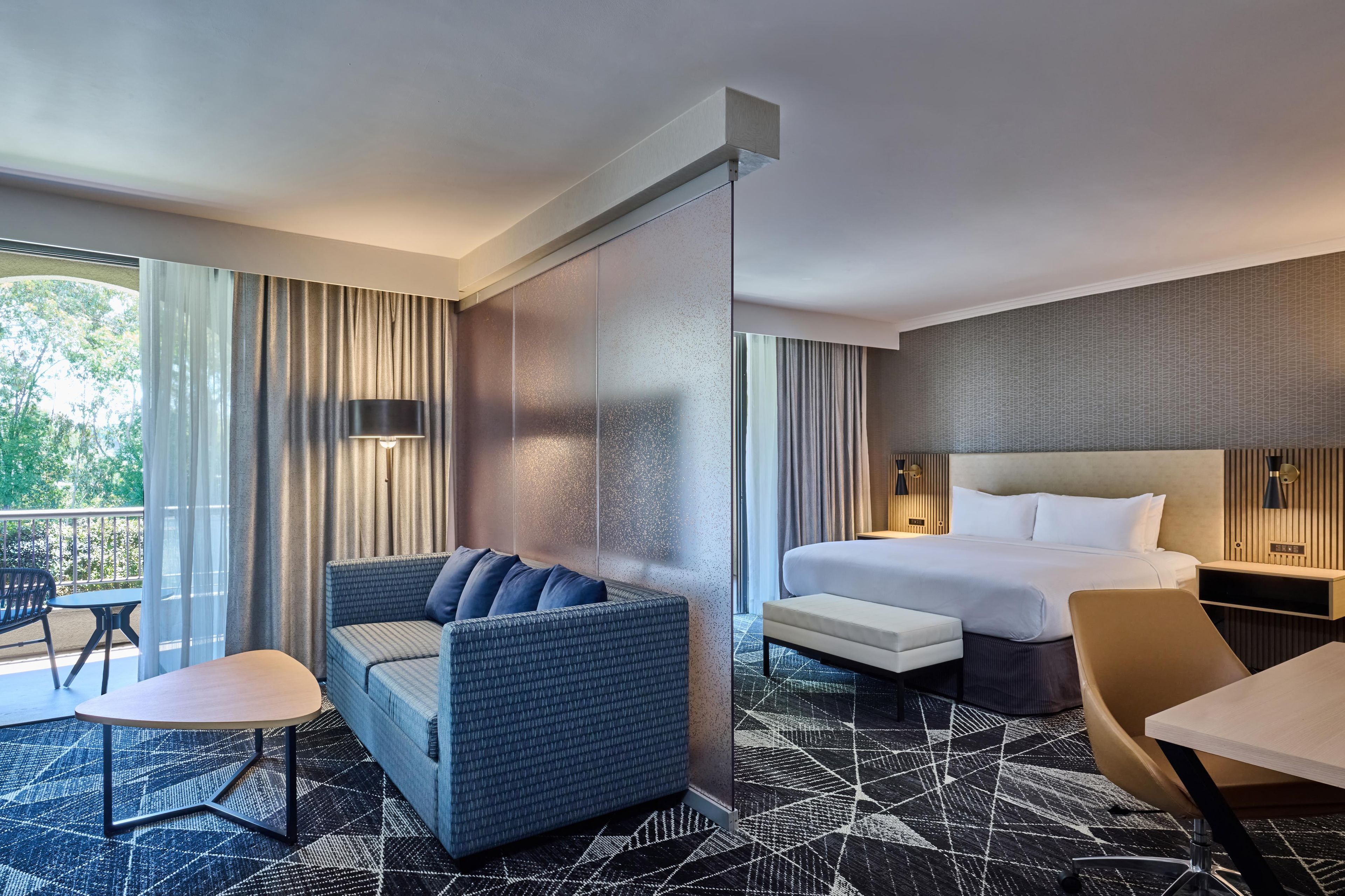 Une chambre d’hôtel avec un lit, un canapé, une chaise, une petite table et un balcon avec vue.