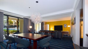 A hotel room with a large dining table, comfortable seating, a sofa, a TV, and a view of the outdoors. - Doubletree by Hilton Newark - Fremont (Newark)