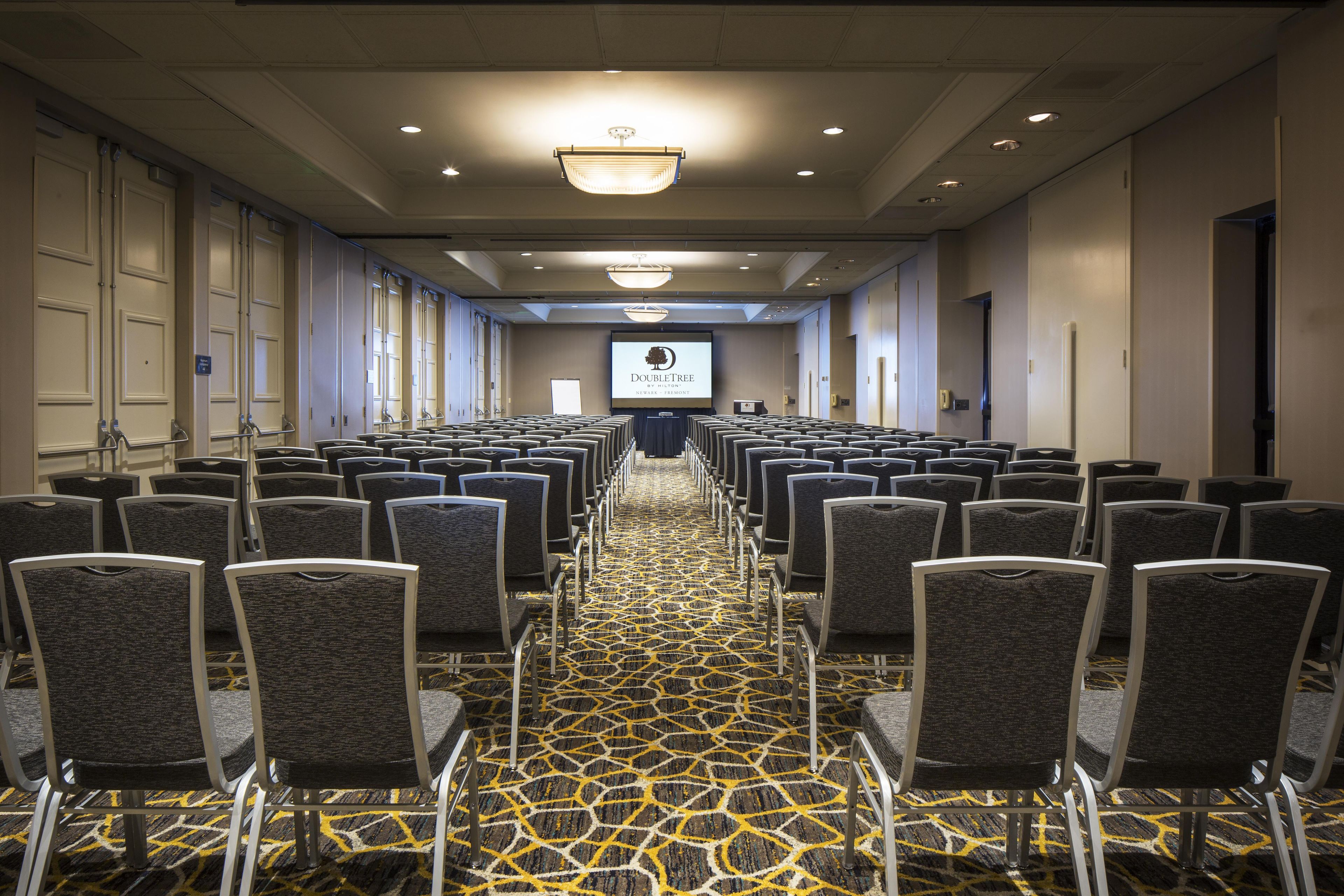 A conference room with rows of chairs, a projector screen, and a carpeted floor.