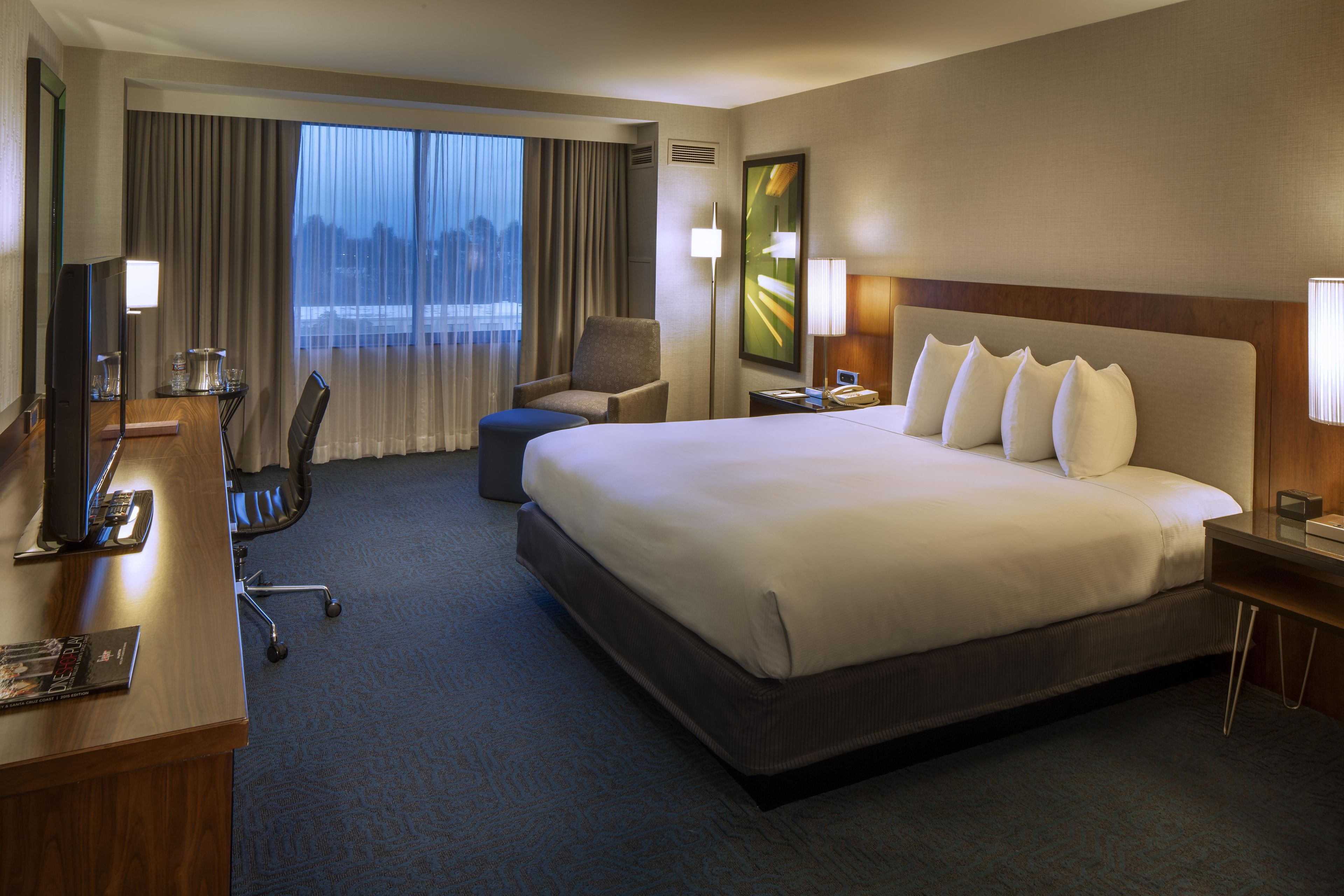 A hotel room with a large bed, a desk, a chair, a television, and a window with curtains.