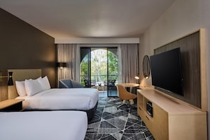 Habitación de hotel con dos camas, televisión, escritorio y balcón con vistas.