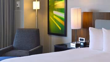 Une chambre d’hôtel avec un lit, une chaise, une table de chevet avec une lampe et un téléviseur fixé au mur.