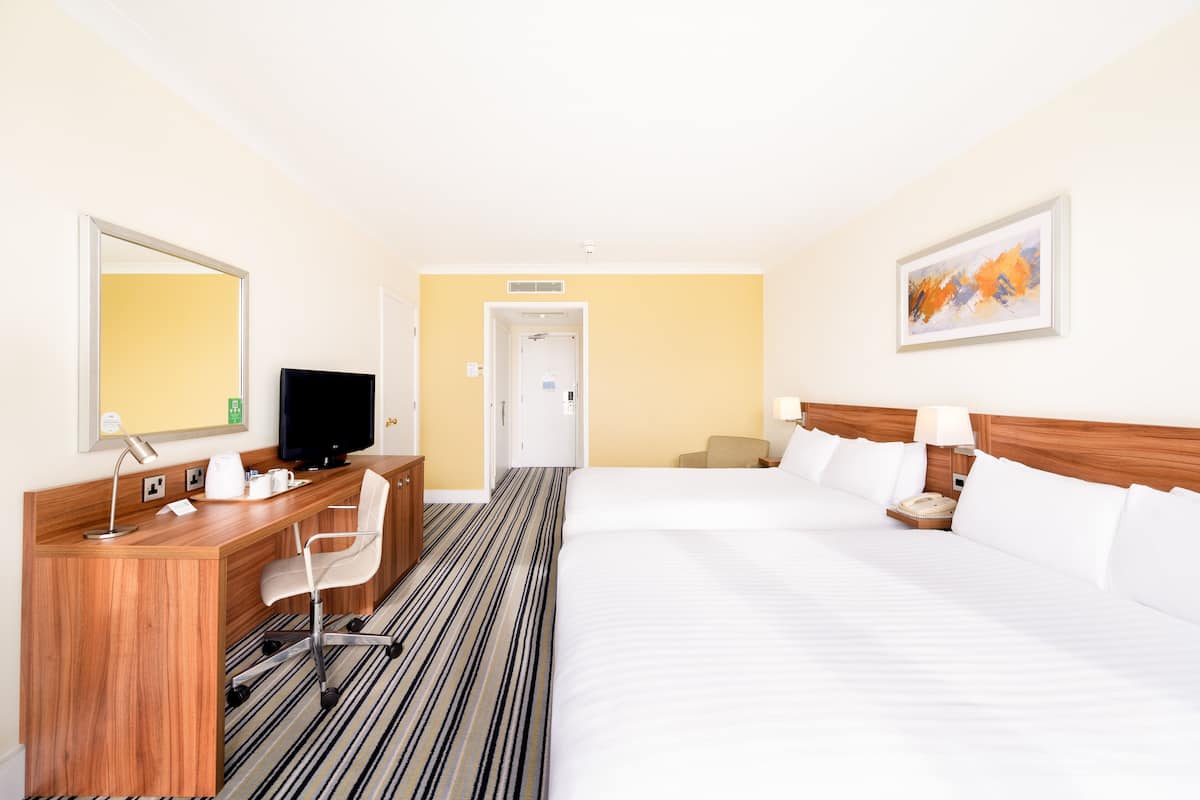 A hotel room with a bed, a desk with a chair, a television, and a painting on the wall.
