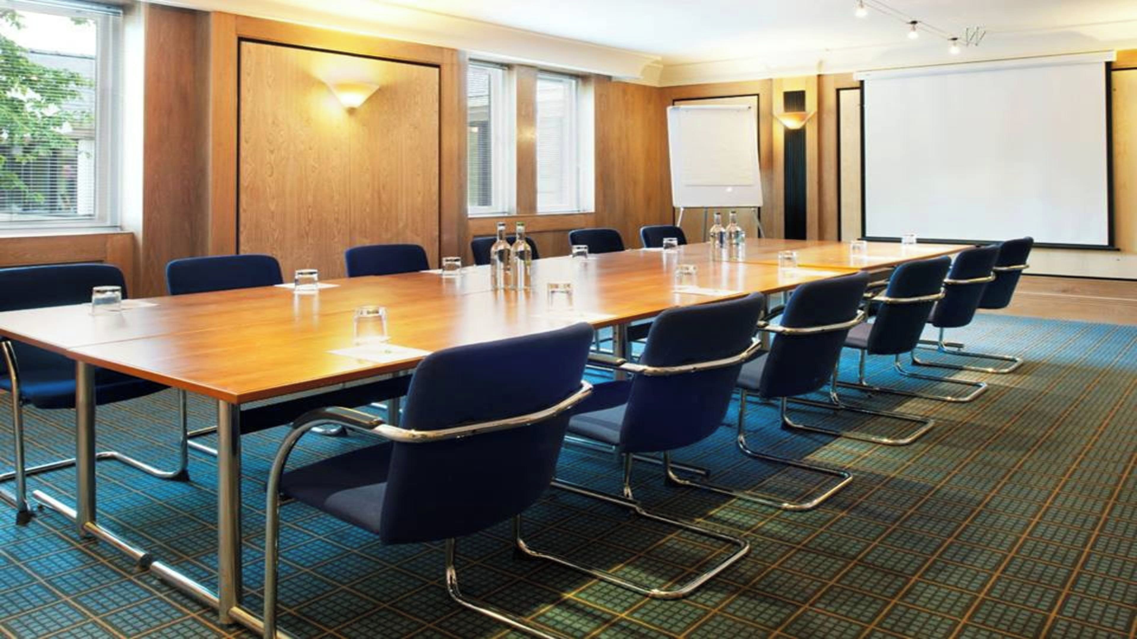 A conference room with a long table, chairs, a projector screen, and a whiteboard.