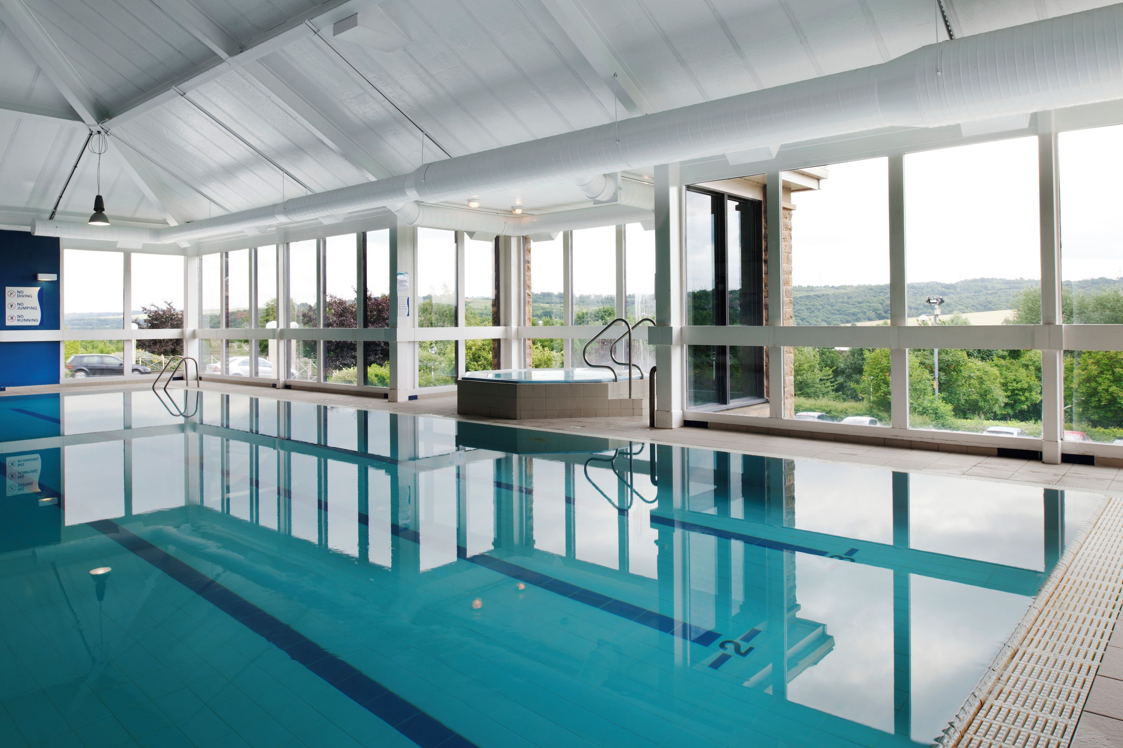 An indoor swimming pool with clear glass walls, a view of the outdoors, and a no diving sign.