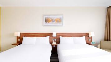 Habitación de hotel con dos camas, cabecera de madera, lámparas de noche, mesita de noche con un teléfono y un cuadro en la pared.
