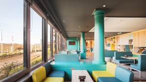 A modern interior with teal and yellow seating, large windows, and a view of the outside. - Holiday Inn Brighouse by IHG (Brighouse)