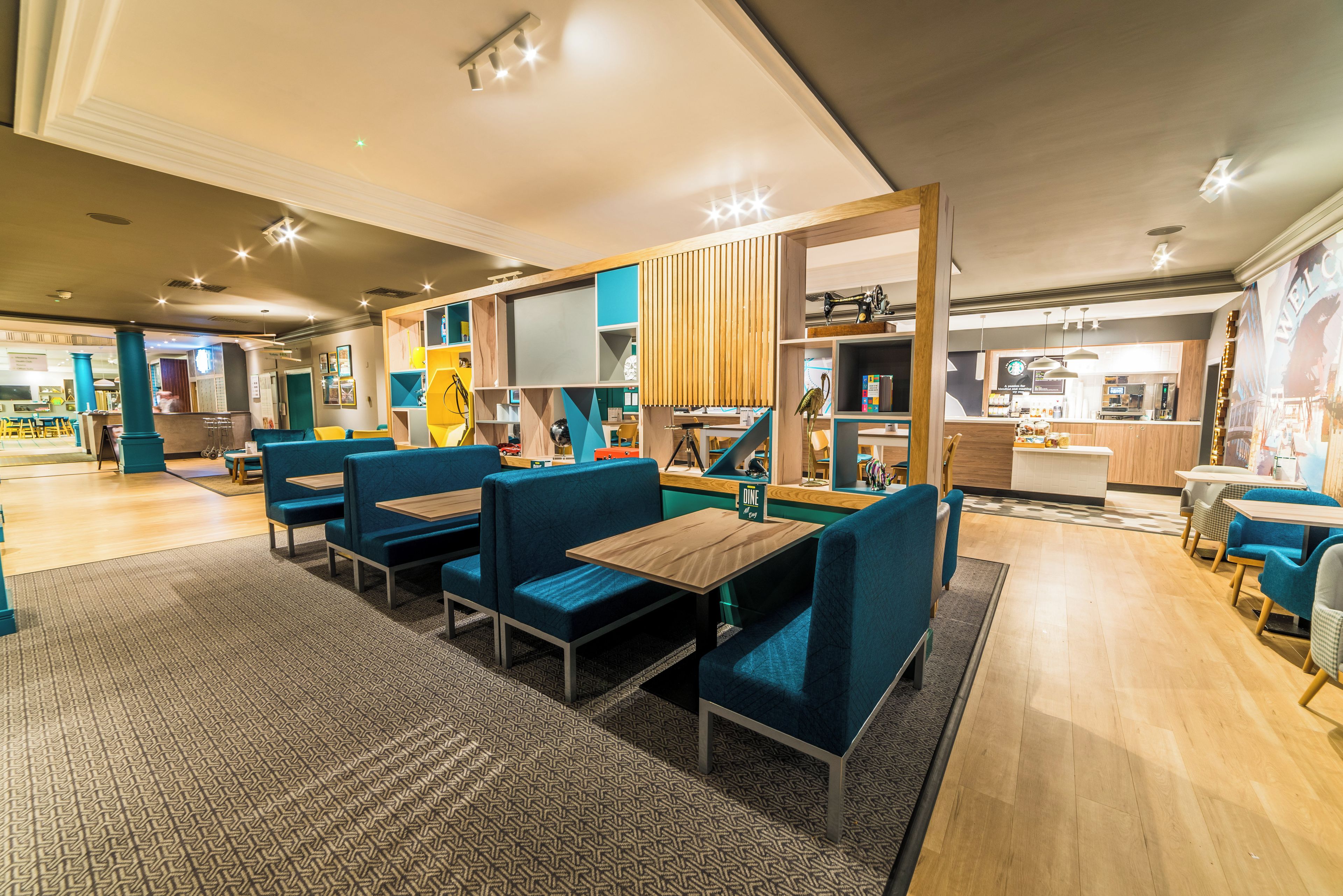 Un restaurante moderno con asientos tipo cabina en azul y mesas de madera, una zona de cocina y una barra.