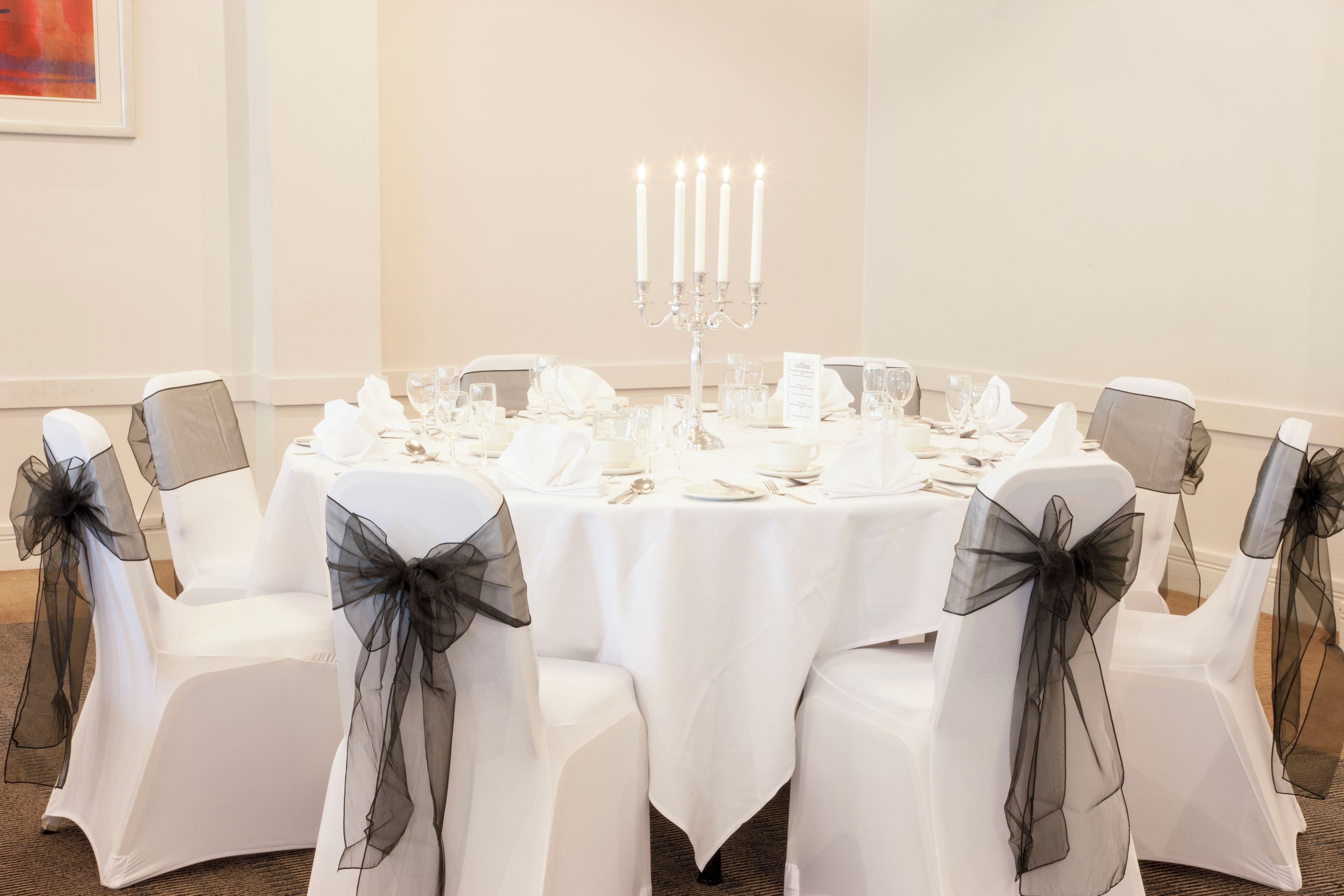 A round table set for a meal with white tablecloth, glassware, and cutlery.