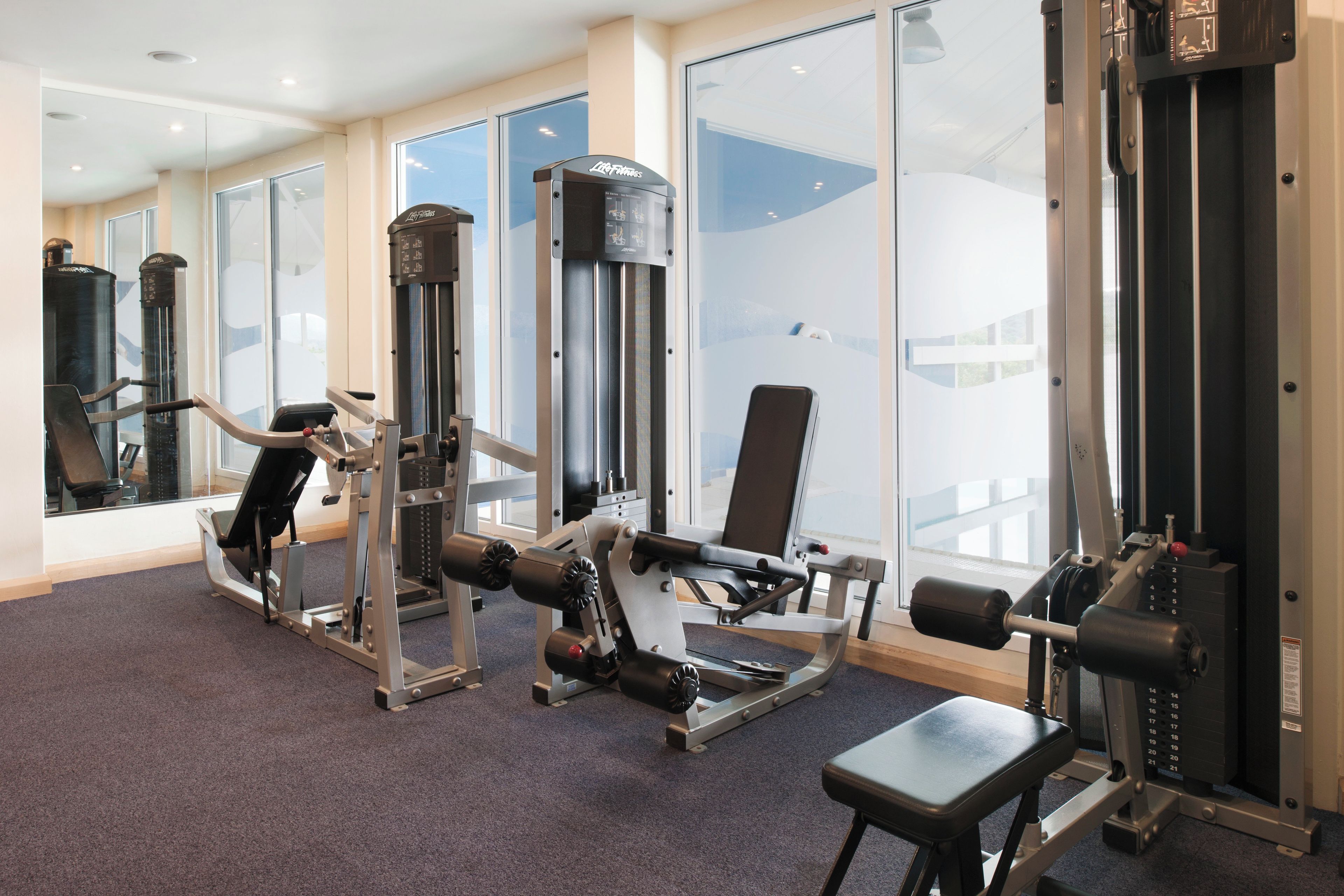 Un gimnasio con diversos equipos de ejercicio, incluyendo una máquina para prensa de piernas, una máquina para prensa de pecho y una jaula para sentadillas.