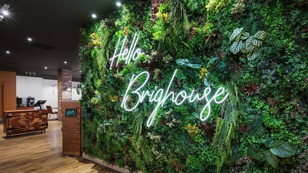 A reception area with a lush green wall, a neon 'Hello Brisbane' sign, and a wooden reception desk. - Holiday Inn Brighouse by IHG (Brighouse)
