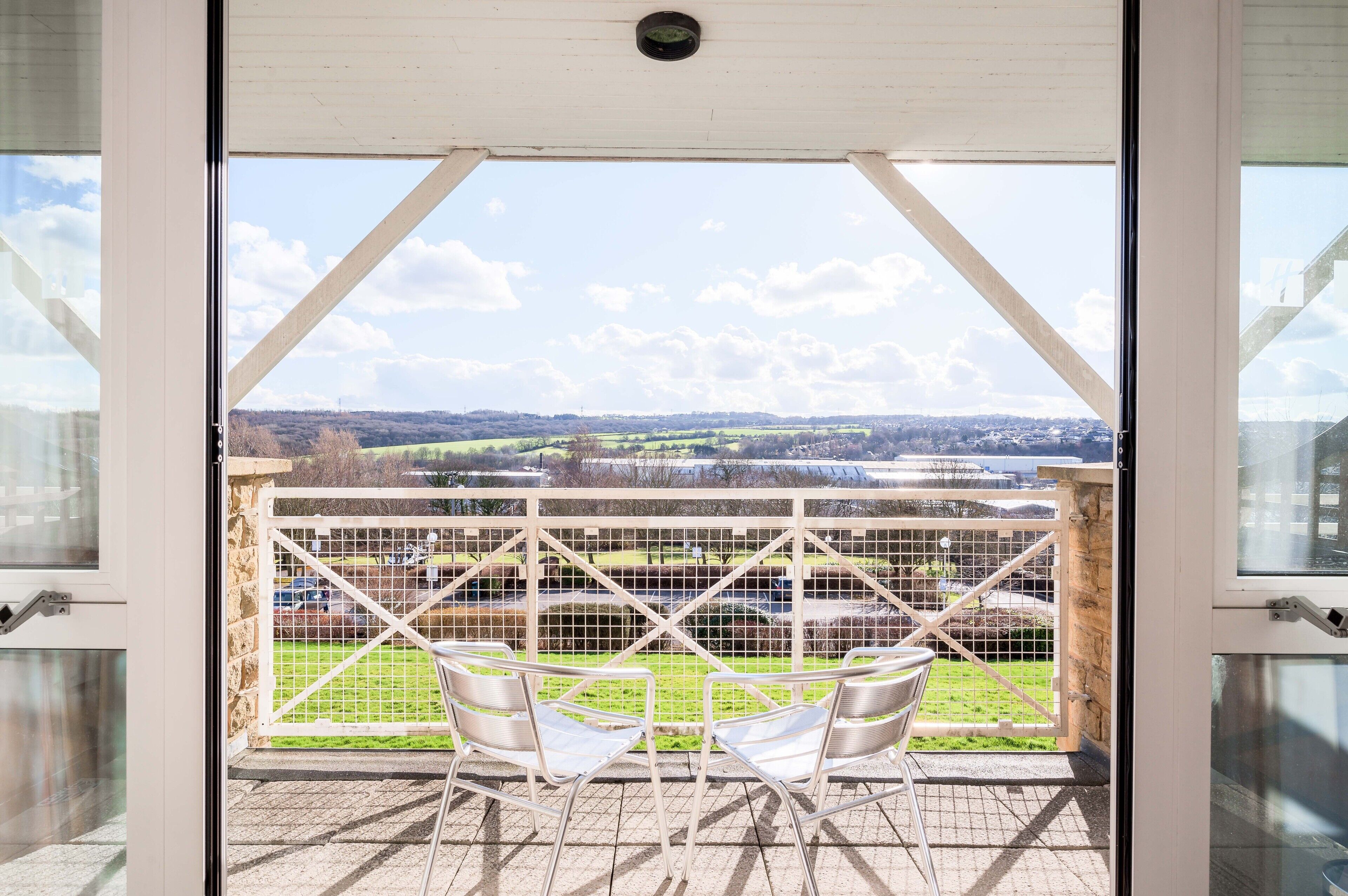 A balcony with two chairs and a view of a green landscape.