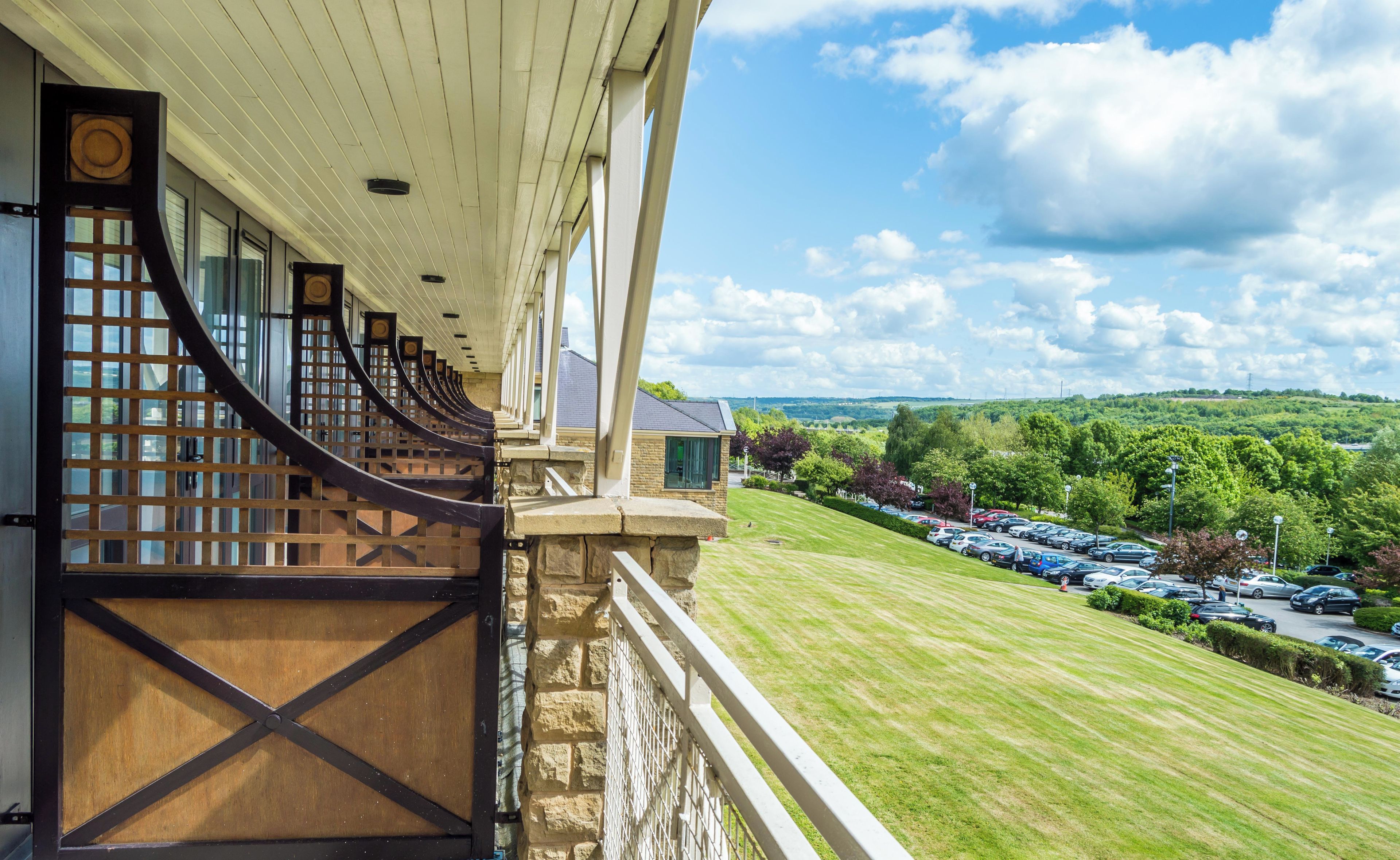 A balcony with a view of a parking lot and a green landscape.