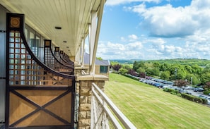A balcony with a view of a parking lot and a green landscape.