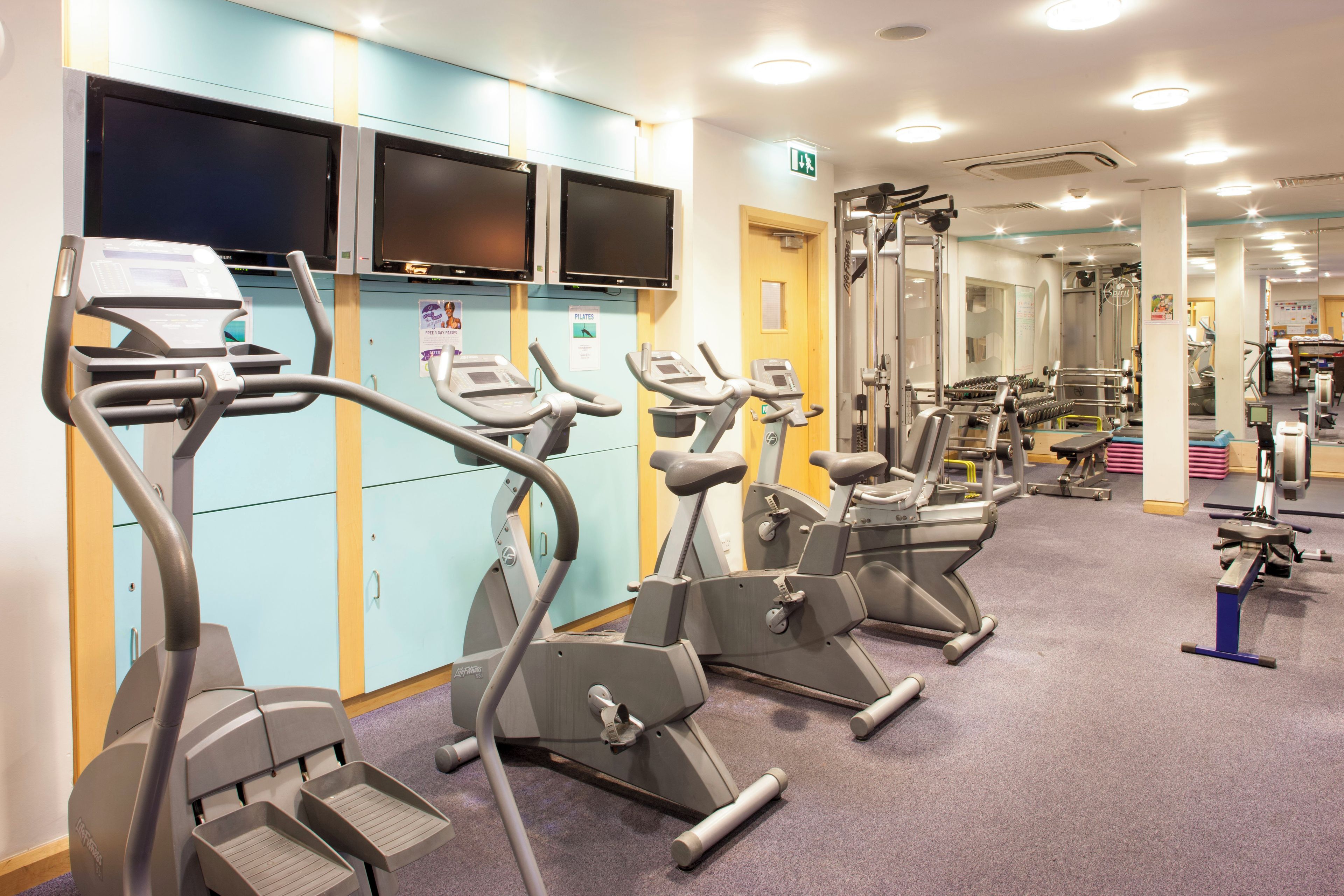 Un gimnasio con varias máquinas de ejercicio, incluyendo cintas de correr y elípticas, dispuestas en filas.