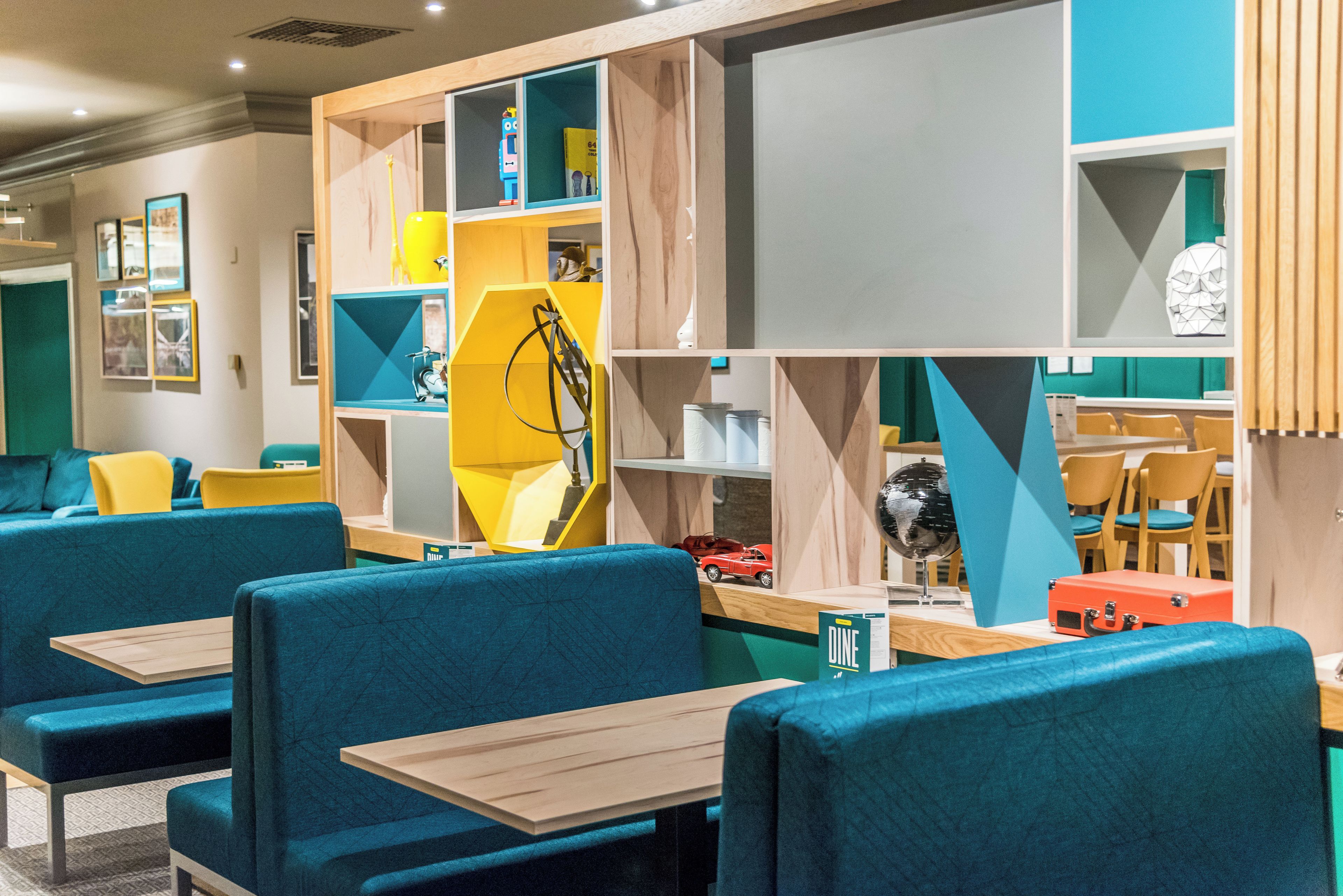 Un intérieur moderne avec des banquettes recouvertes d’un tissu turquoise, des tables en bois et des meubles de rangement aux couleurs vives.